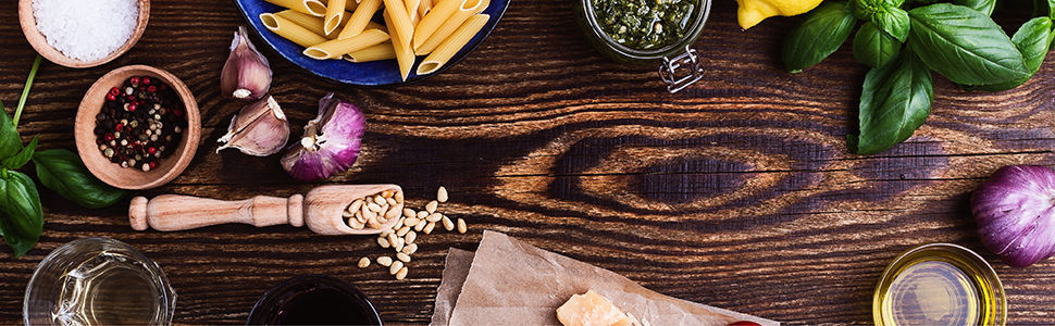 Bird eye view of wood counter with pasta, basil, oil, and herbs